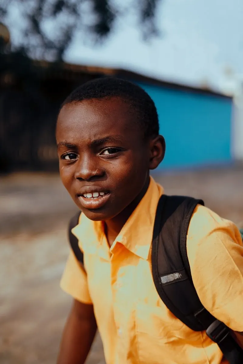 A Rwandan schoolboy with a backpack looking ahead with quiet confidence