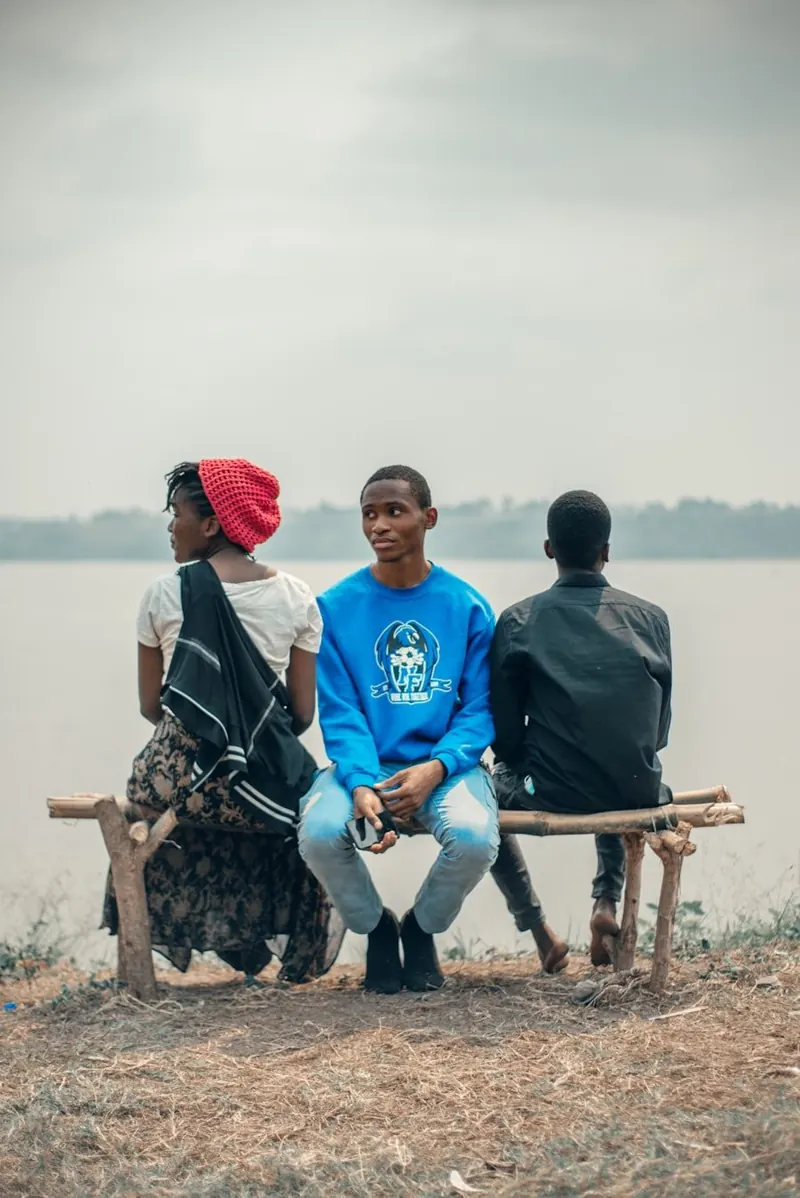 Three young people sitting together on a bench looking out over water